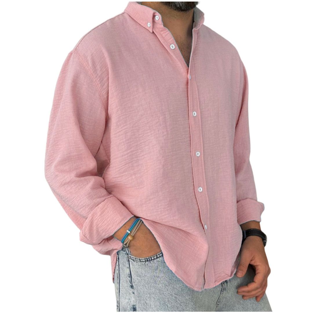 A man wearing a long sleeve button-down blue linen shirt with a collar, rolled up sleeves, and paired with light-colored pants.