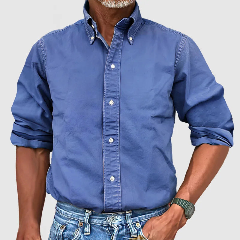 A man wearing a beige button-down shirt with the sleeves rolled up to the elbows, paired with blue jeans.