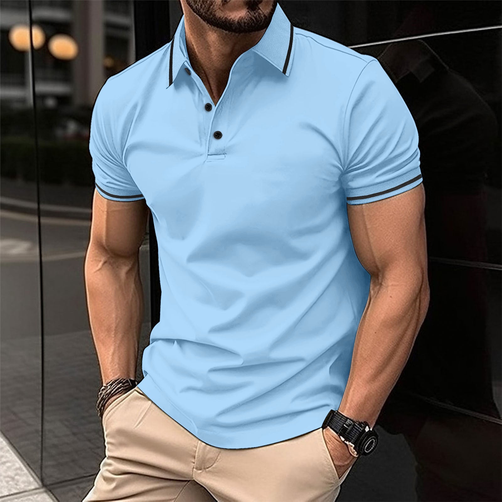 A man wearing a blue polo shirt with contrast trim around the collar and sleeves, standing in a reflective indoor setting.