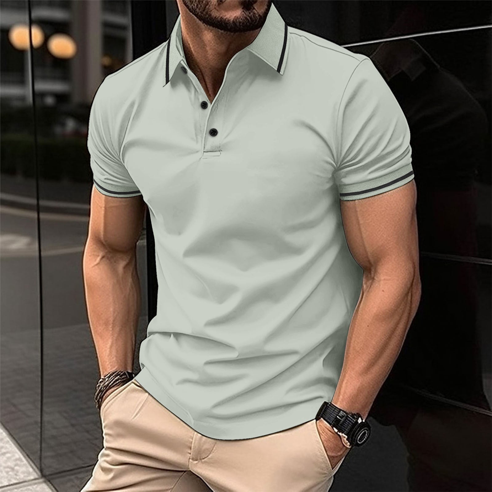 A man wearing a green polo shirt with contrast trim around the collar and sleeves, standing in a reflective indoor setting.