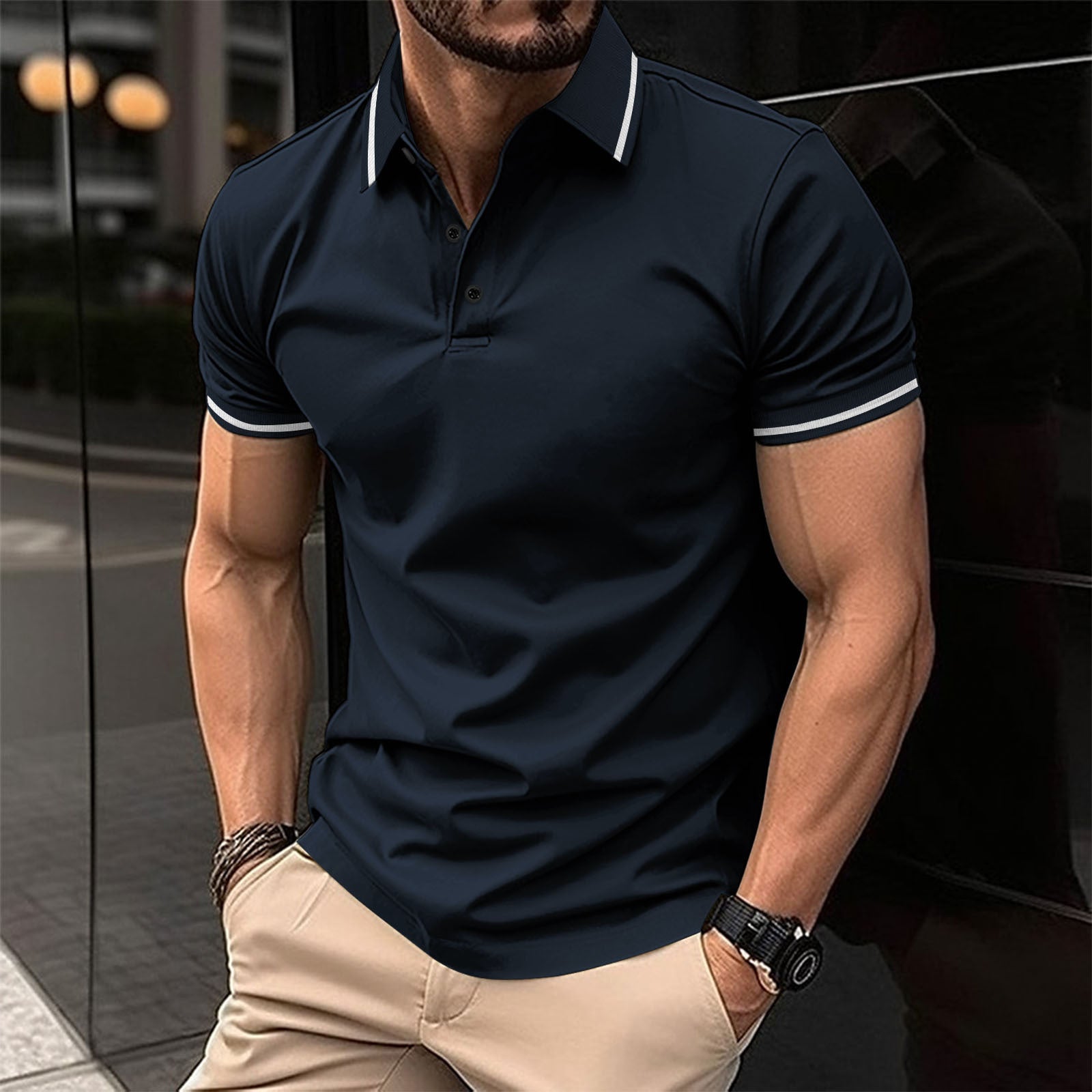 A man wearing a navy polo shirt with contrast trim around the collar and sleeves, standing in a reflective indoor setting.