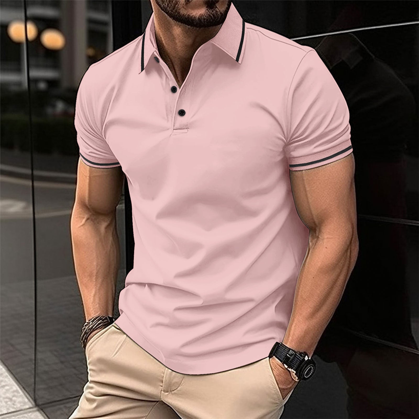 A man wearing a pink polo shirt with contrast trim around the collar and sleeves, standing in a reflective indoor setting.