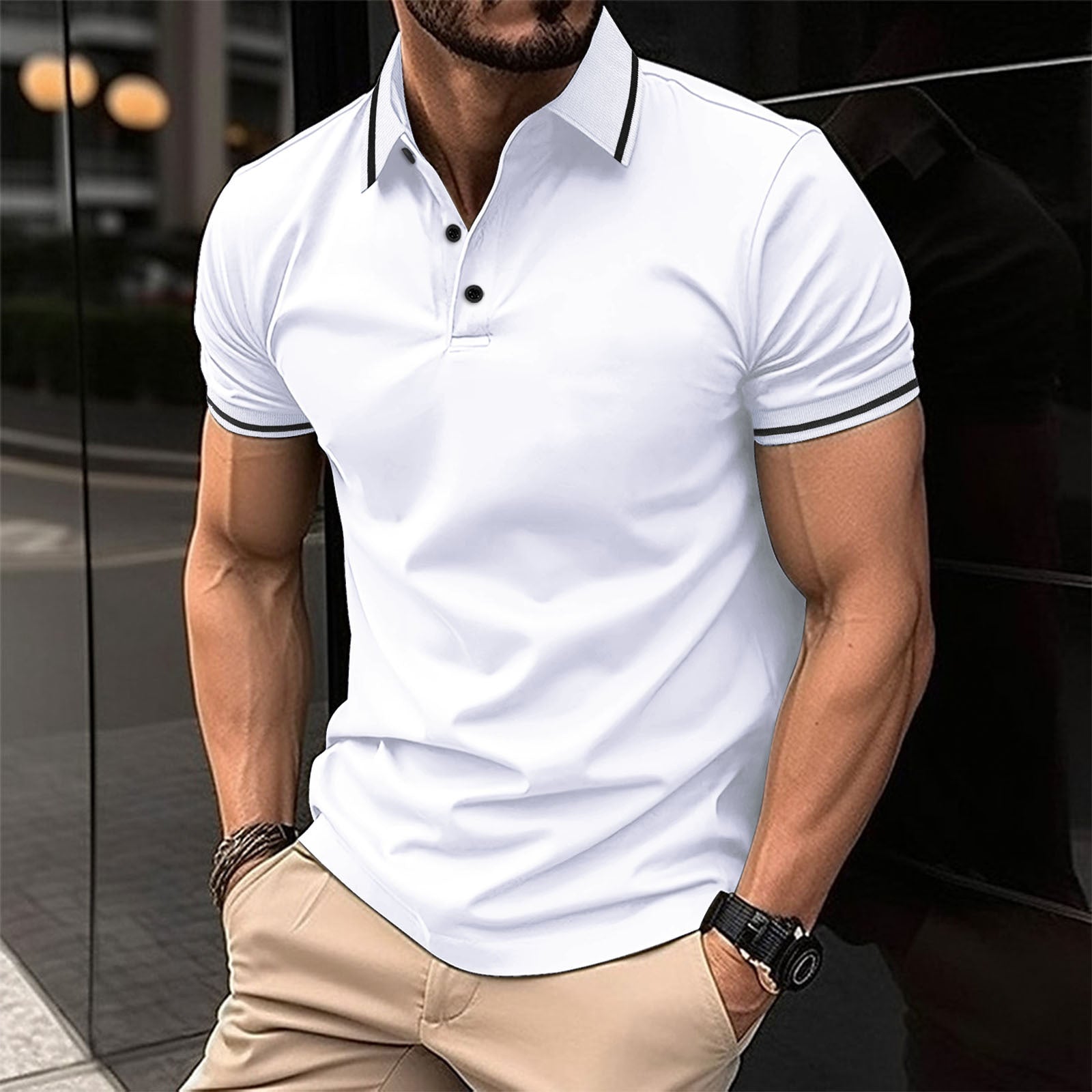 A man wearing a white polo shirt with contrast trim around the collar and sleeves, standing in a reflective indoor setting.