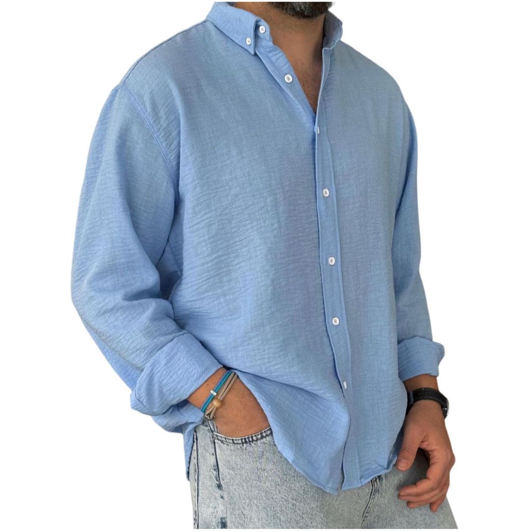 A man wearing a long sleeve button-down blue linen shirt with a collar, rolled up sleeves, and paired with light-colored pants.
