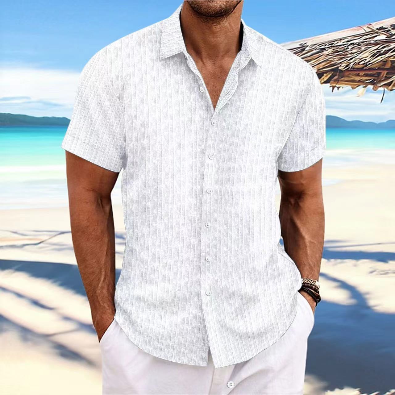 Man wearing a white striped shirt on a beach with clear blue water and sky.