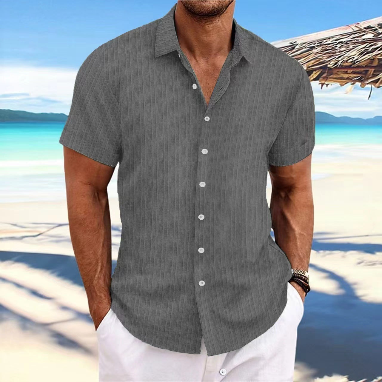 Man wearing a gray striped shirt on a beach with turquoise water and white sand.